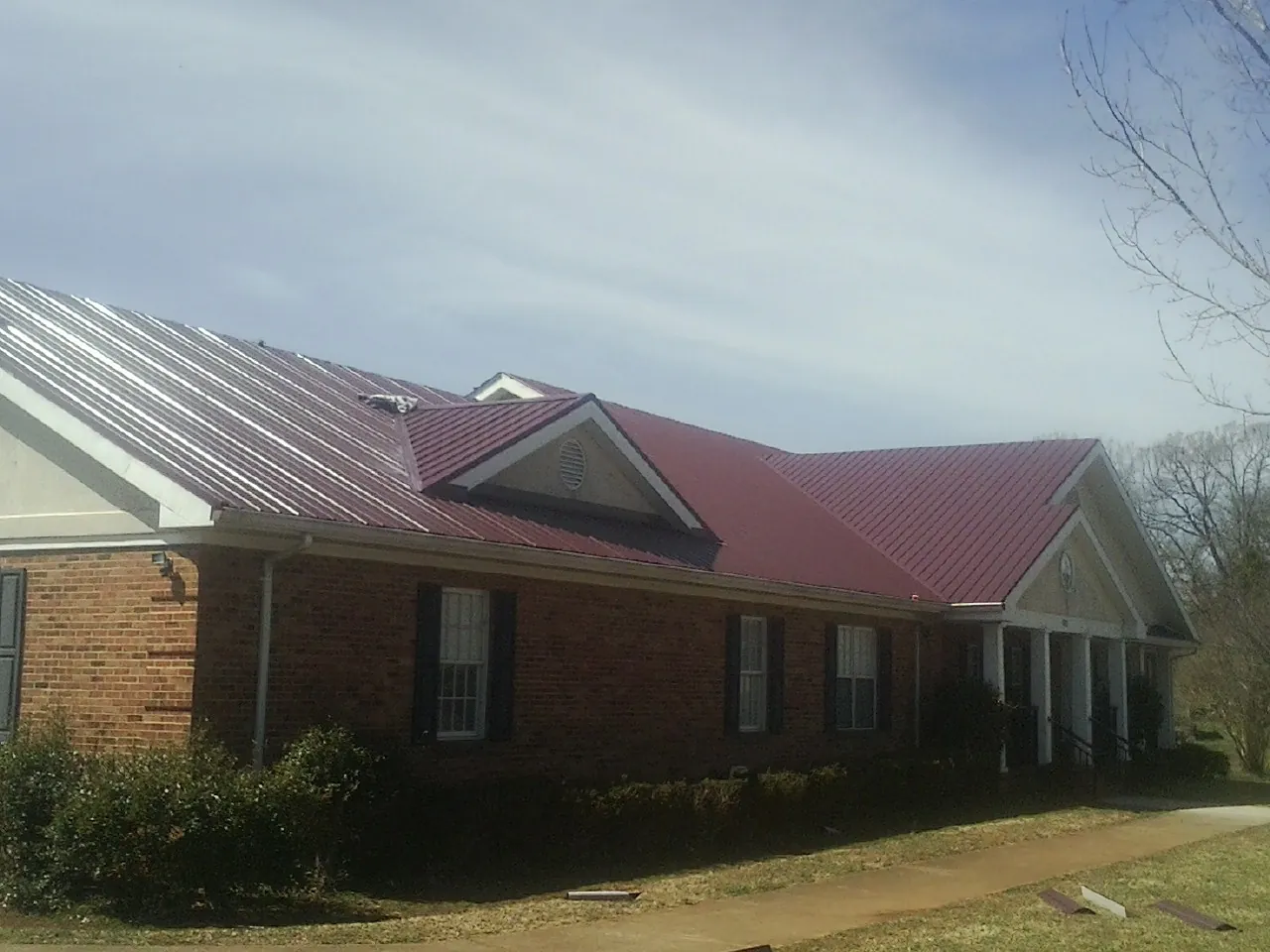 Red metal roof with gabled entries on a long brick building, from a Hail Damage Roof Repair job in South Salem