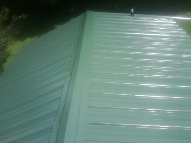 New green metal panels meeting at the ridge of a roof — Flat Roof Repair work by our crew in South Salem