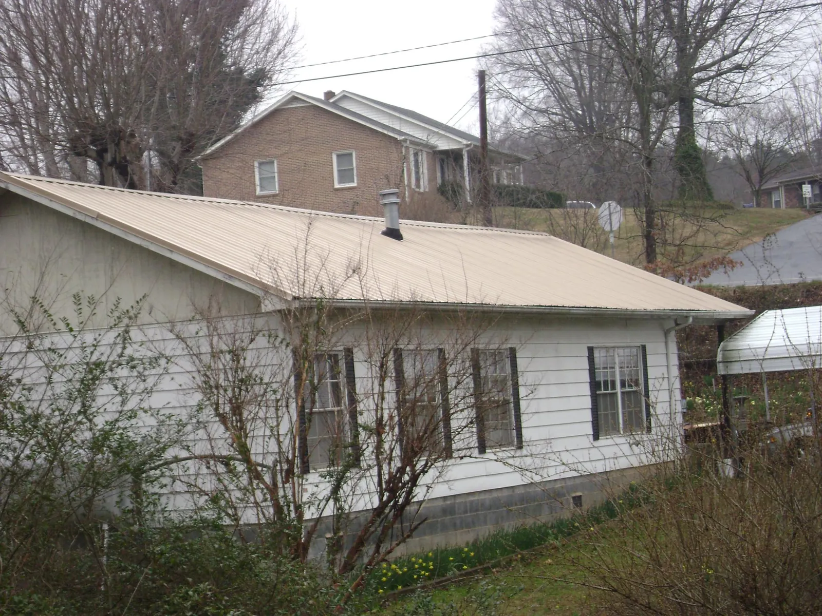 Tan metal roof on a white sided house set into a hillside — Commercial Roofing by Roofing Brothers in South Salem